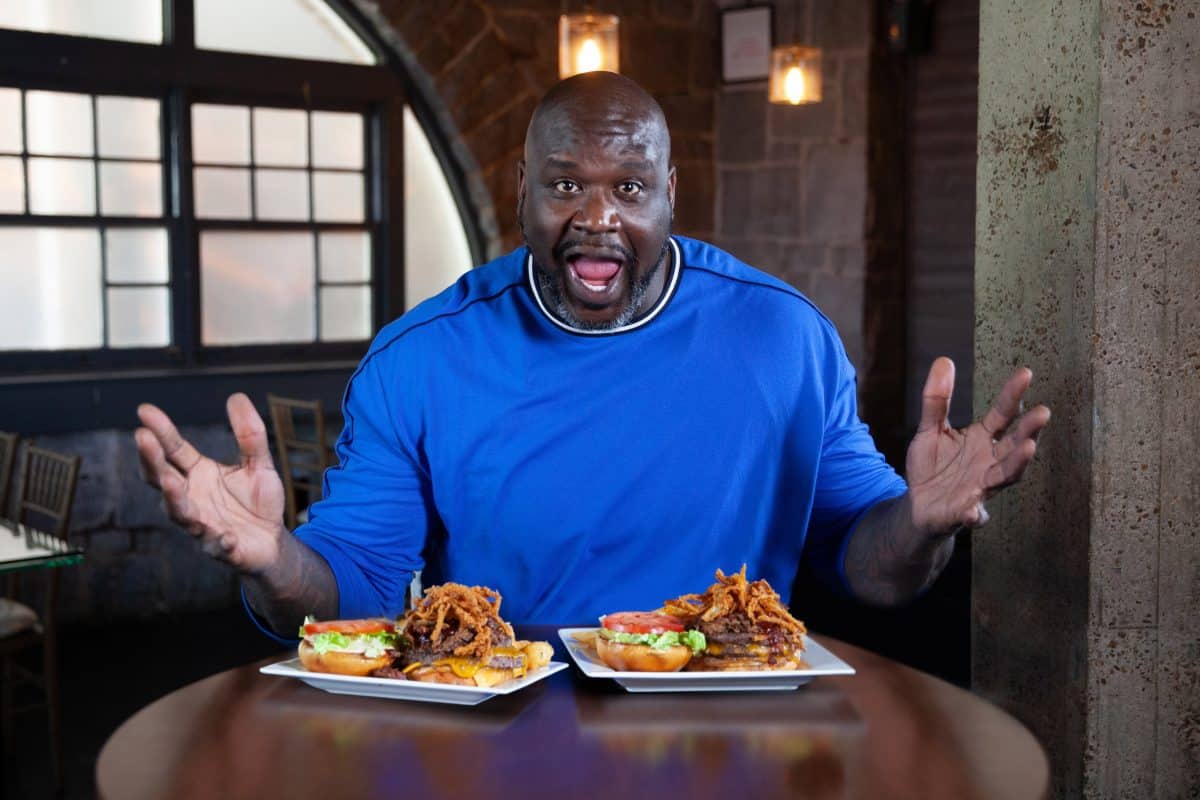 Shaq se sienta en una mesa frente a dos platos con sándwiches.